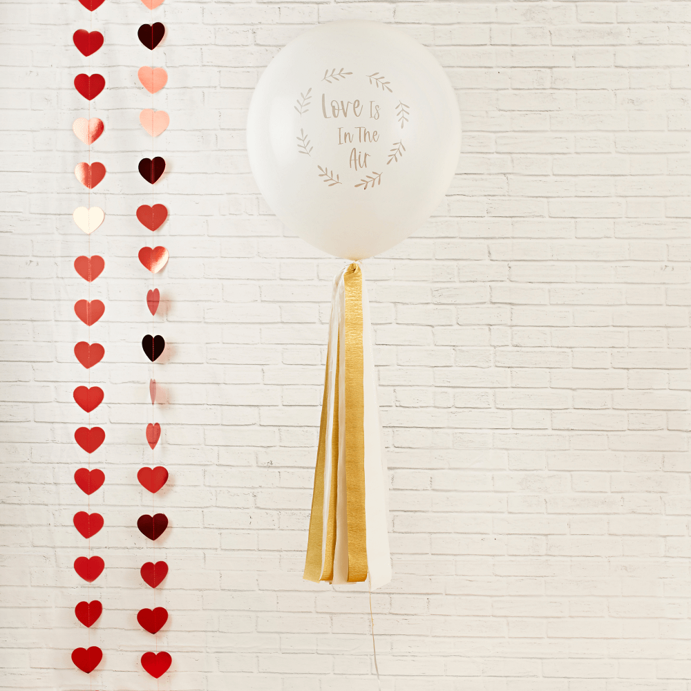 Ballon met gouden tassels en de tekst love is in the air hangt naast een hartjes slinger