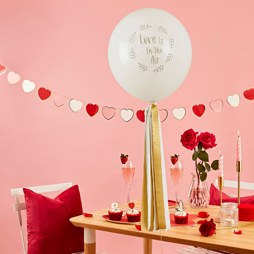 Ballon met gouden tassels en de tekst love is in the air hangt voor een versierde ruimte met valentijns versiering