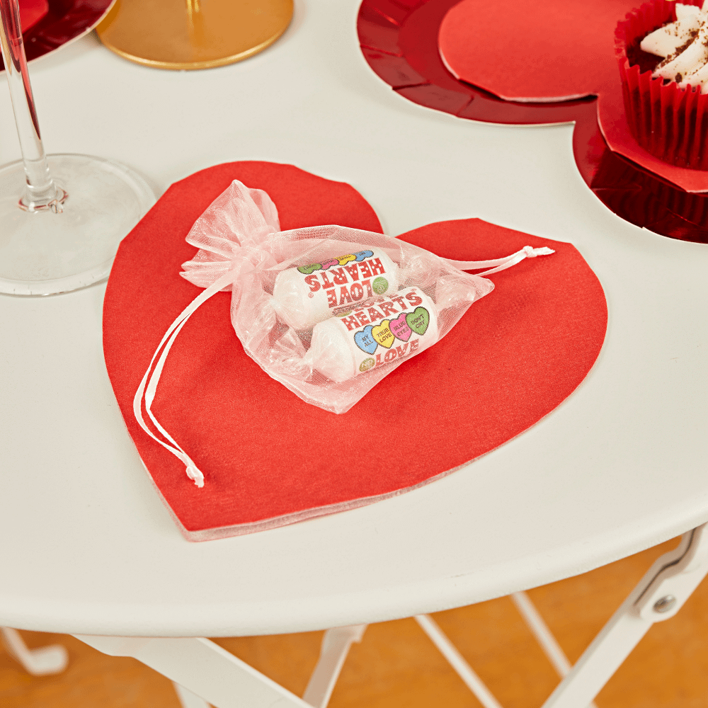 rode servet in de vorm van een hartje ligt op een witte tafel onder een zakje snoep