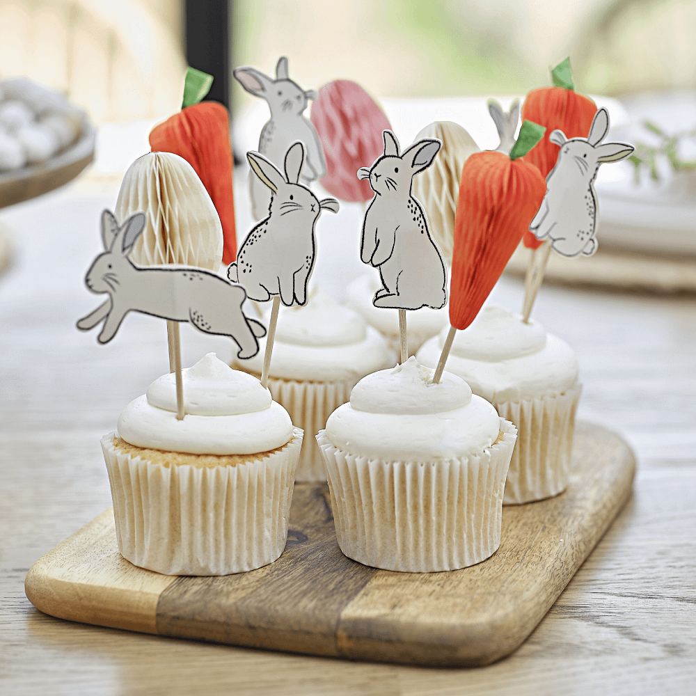 Cupcake toppers voor pasen met een wortel, paasei en konijntjes erop zitten in cupcakes op een hapjesplank