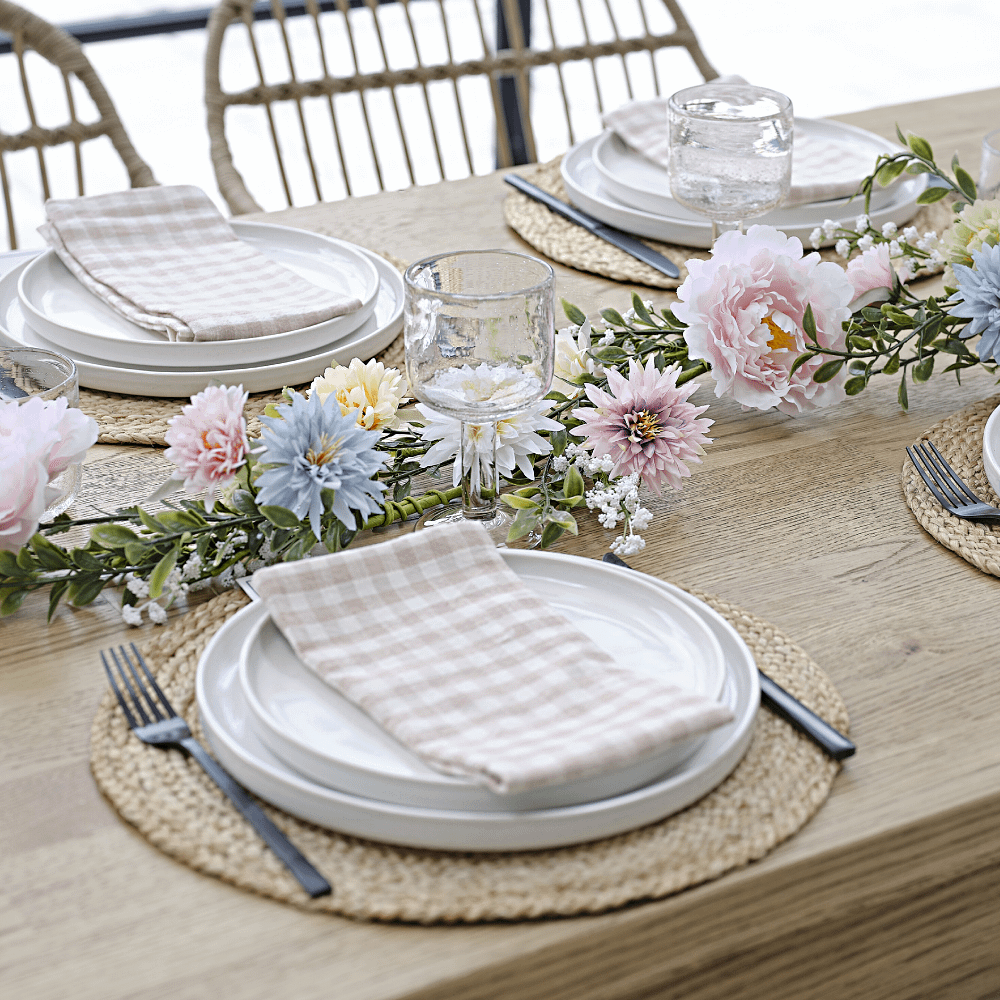 Slinger met kunstbloemen ligt op een houten tafel met roze en wit geblokte servetten