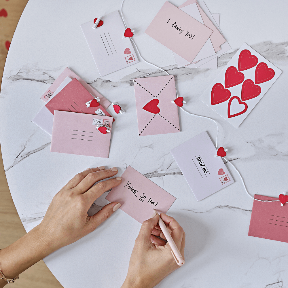DIY slinger voor valentijnsdag met rode, roze en witte enveloppen en wasknijpers met hartjes erop