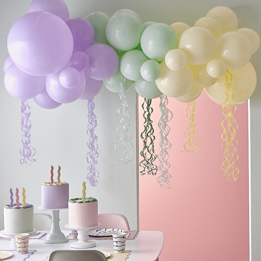 Pastel ballonnenboog met streamers hangt boven een versierde tafel met taarten