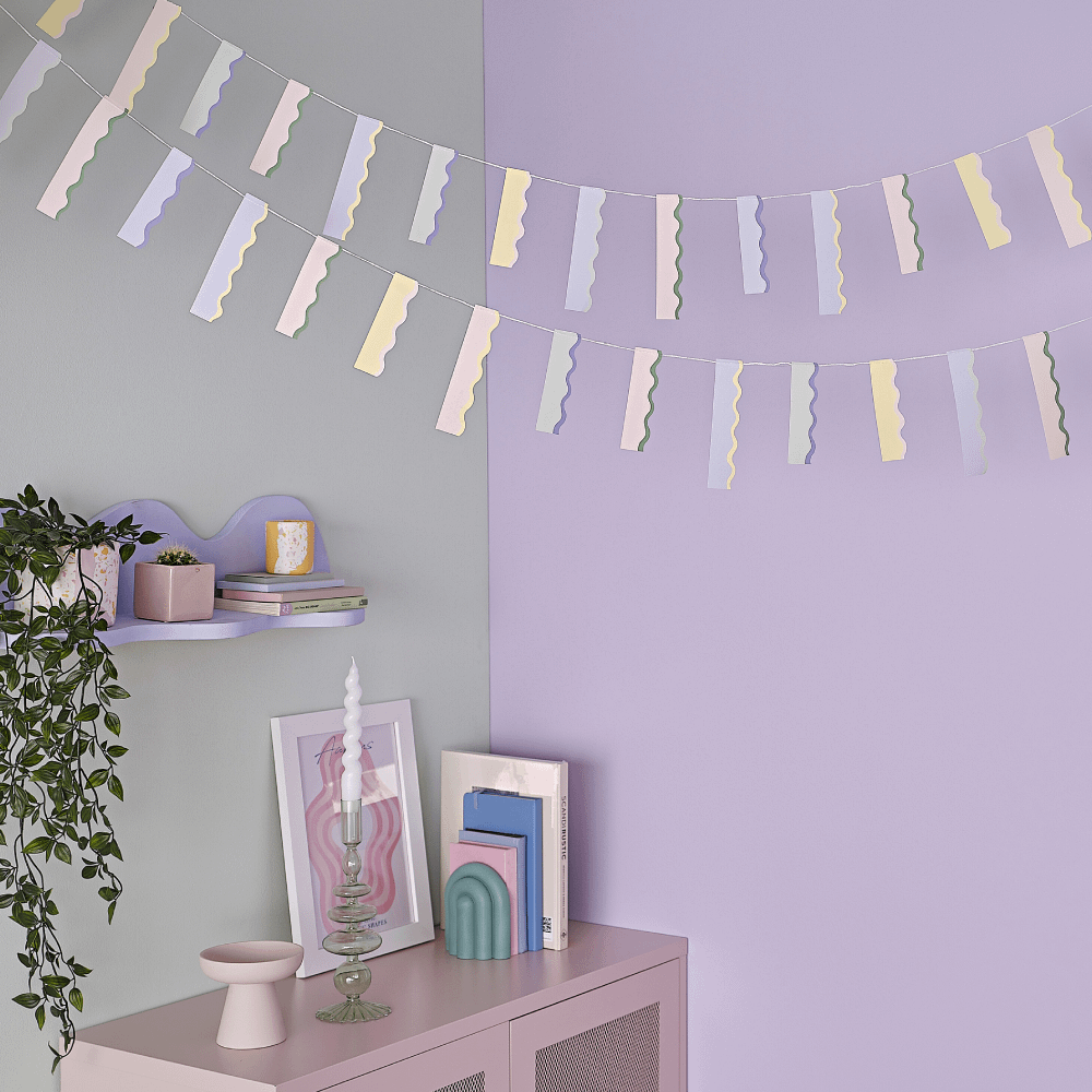 Slinger met golvende vlaggen in pastel tinten hangt voor een lila muur