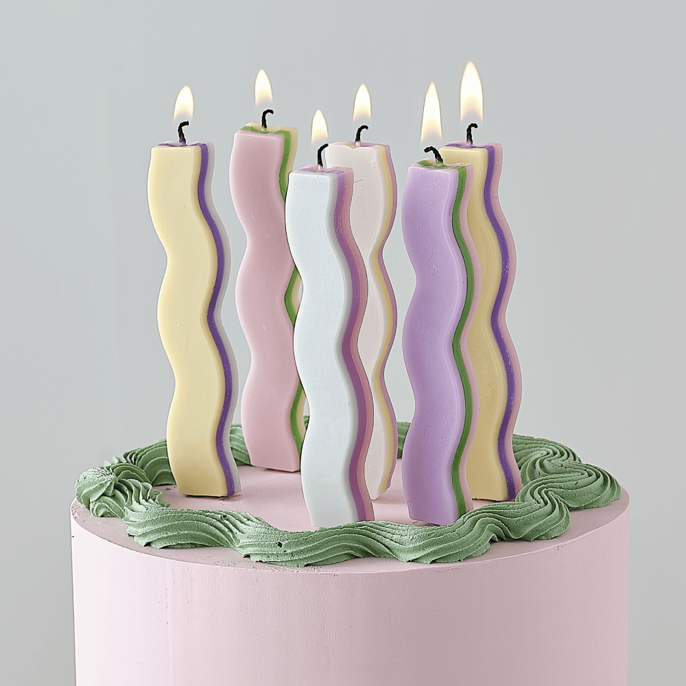 Golvende pastel kaarsen staan op een pastel roze taart