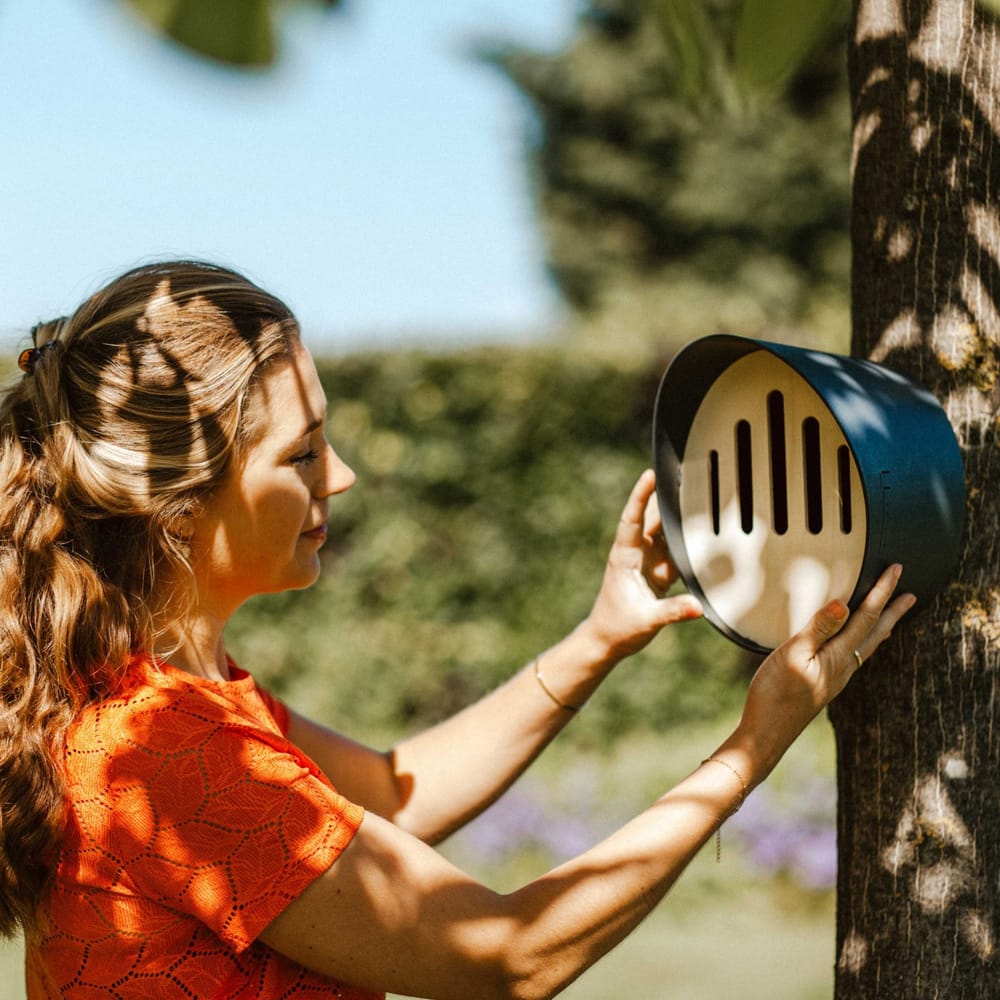 vrouw hangt vlinderhuis met zwarte kunststof buitenkant in boom