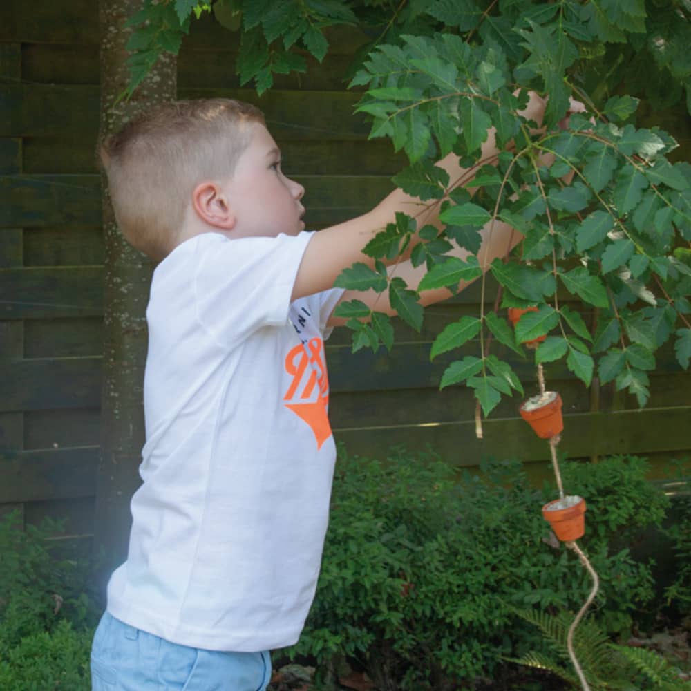 Kind hangt voederslinger met klokjes in boom