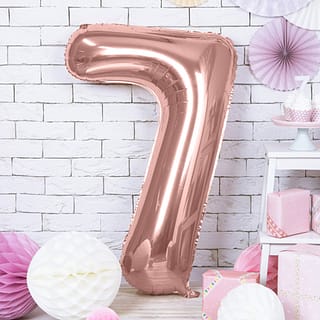 Rosé gouden folieballon cijfer 7 voor een muur met witte bakstenen versierd met witte en roze honeycombs en een paarse waaier