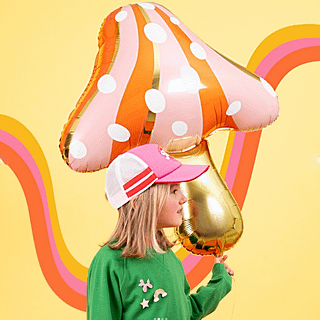 Meisje met roze pet en groene trui houd een ballon vast in de vorm van een paddenstoel voor een gele achtergrond