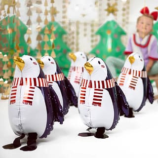 Vijf folieballonnen in de vorm van pinguins met in de achtergrond een meisje en kerstboompjes