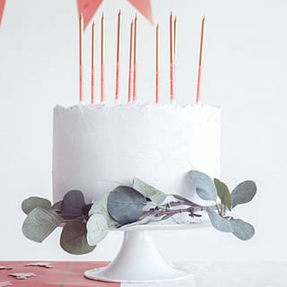 Witte taart met rose gouden kaarsen en versierd met blaadjes