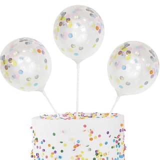 Drie stokjes met ballon erop gevuld met confetti in taart