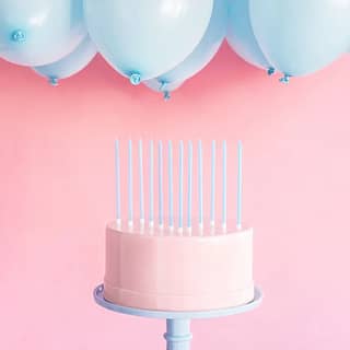 Zes lange lichtblauwe taartkaarsen op een taart met ballonnen erboven