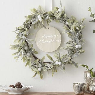 Kerstkrans met witte details en houten plaatje in het midden met merry christmas erop
