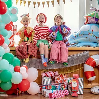 Drie kinderen in kamer met ballonnenboog en cadeautjes