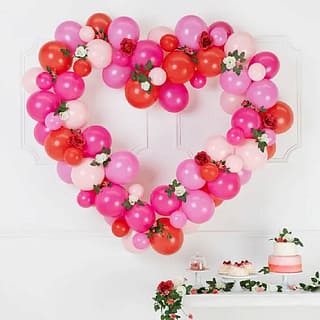 Ballonnenframe in de vorm van een hart in de kleuren rood, roze en lichtroze boven een tafel met een rozenslinger