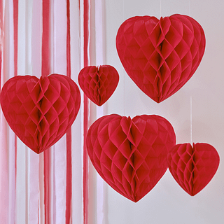 Rode honeycombs in de vorm van hartjes hangen aan een wit draad aan het plafond voor een roze met rode backdrop