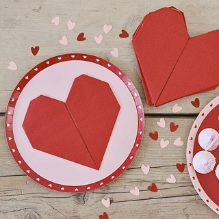 Papieren bordjes met een rode rand met roze hartjes en rode hartvormige servetten op een houten tafel met hartjes confetti