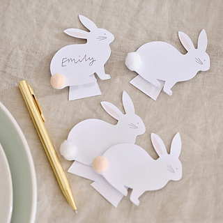 Kartonnen konijntjes met lichtroze staart op een beige tafelkleed liggen naast een gouden pen