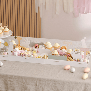 Tafel met een witte hapjesplank met konijntjes en wortels, versierd met paaseieren, marshmallows en macarons