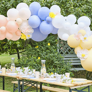 Versierde picknicktafel met bloemen en een pastelkleurige ballonnenboog