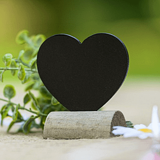 Krijtbord in de vorm van een hartje in een houten standaard staat op tafel naast madeliefjes en eucalyptus
