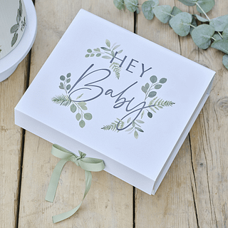 Cadeaudoosje in het wit met groene bladeren ligt op een houten tafel naast eucalyptusblaadjes