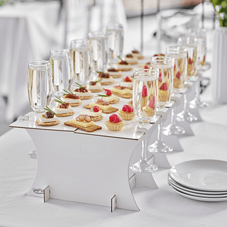 Hapjes en drankjesstandaard met champagneglazen en crackers met kaas staat op een witte tafel naast witte schaaltjes