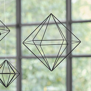 Zwarte metalen hanger met geometrische vormen hangt voor een raam met zwarte kozijnen