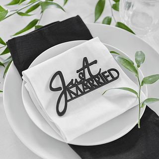 Witte borden met zwart servet en zwart bordje met de tekst just married staan op een wit tafelkleed versierd met groene takjes