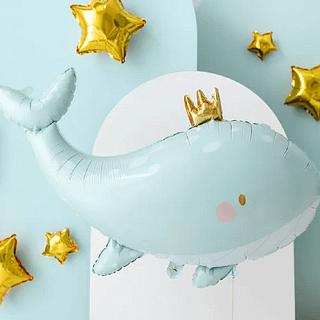 Folieballon in de vorm van een walvis met een gouden kroontje op een lichtblauwe en witte achtergrond met gouden sterren