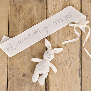 Sjerp met de tekst mummy to be ligt op een houten vloer naast een wit knuffelkonijntje