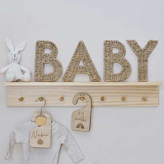 Rieten letters BABY staan op een houten plank naast een wit konijntje