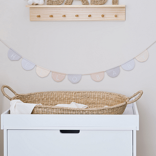 Babykamer versierd met een stoffen slinger, houten plank met haakjes en rieten mandje met wit dekentje