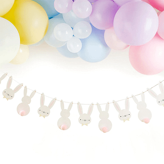 Slinger met schattige konijntjes met lichtroze pompoms hangt onder een ballonnenboog met paarse, blauwe en gele ballonnen in pasteltinten