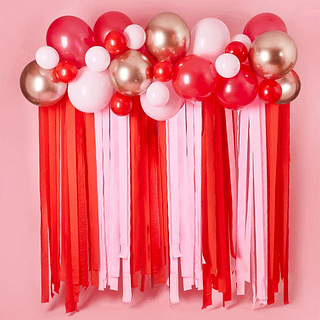 Ballonnenboog in het rose goud, roze en rood met roze en rode streamer s hangt voor een roze muur