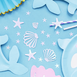 Iridescent confetti in de vorm van zeesterren en schelpen liggen op een lichtblauwe ondergrond