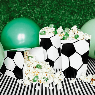 Popcornbakjes met voetbalprint zijn gevuld met popcorn en groene snoepjes en staan op een wit met zwart gestreepte ondergrond