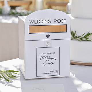 Witte doos in de vorm van een brievenbus met zware tekst staat op een witte tafel voor een bruiloftstaart