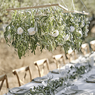 Houten rooster hangt boven een witte tafel en is gevuld met bloemen en planten