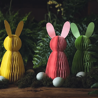 Drie honeycombs in het geel, groen en roze in de vorm van konijntjes staan in een laagje mos versierd met gestippelde paaseieren
