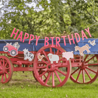 Slinger met rode letters happy birthday en boerderijdieren zoals een paard, eend, varken, schaap, koe, hond en tractor hangt boven een grasveld voor een huifkar