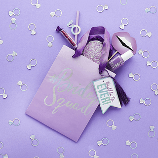 Paars cadeaytasje met iridescent tekst is omringd met confetti in de vorm van trouwringen