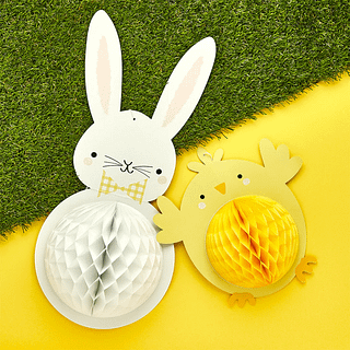 Honeycombs in de vorm van een geel kuiken en een wit konijn liggen op een gele ondergrond met een groene grasmat