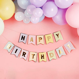 Pastelslinger met de gouden tekst happy birthday hangt voor een lichtroze muur onder ballonnen in pasteltinten