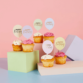 Cocktailprikkers in de vorm van ballonnen in pasteltinten met de tekst happy birthday zitten in cupcakes en staan voor een roze, blauwe en pastelgroene achtergrond