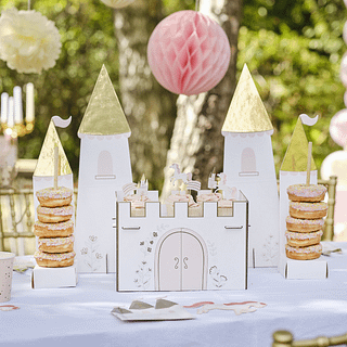 Hapjesstandaard in de vorm van een kasteel met roze en gouden kleuren staat op een witte tafel onder een roze honeycomb