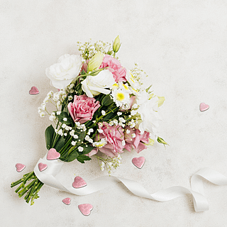 Bosje bloemen met witte en roze rozen en madeliefjes ligt op een wit kleed met confetti hartjes