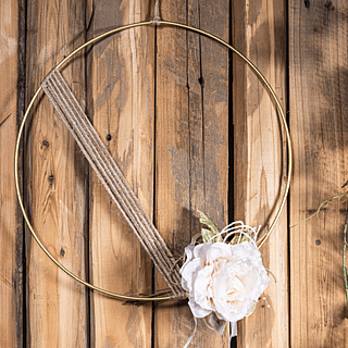 Gouden cirkeln van metaal met jute touw en een bloemetje hangt voor een houten schutting