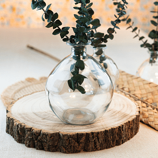 Houten plaat in de vorm van een boomstam staat onder een glazen vaas gevuld met groene bladeren